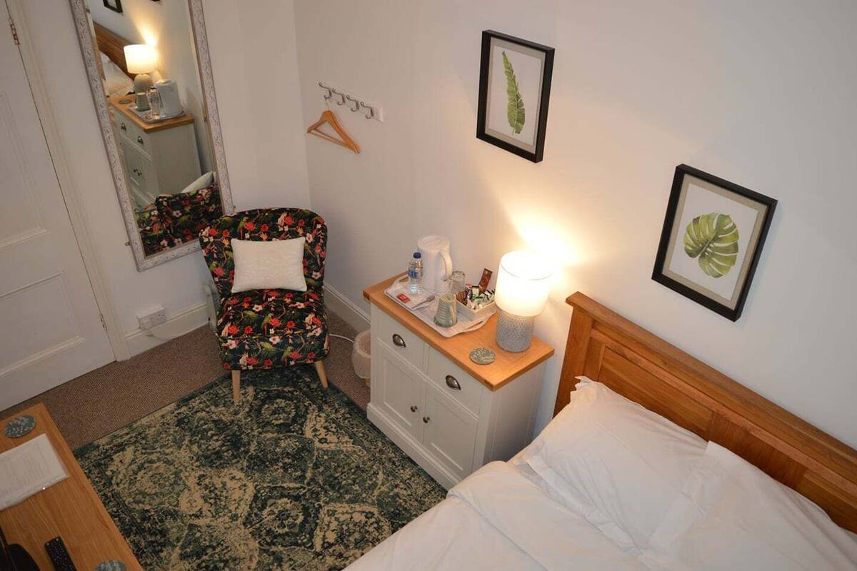 A hotel room with a bed, a chair, a nightstand, a mirror, and framed pictures on the wall.