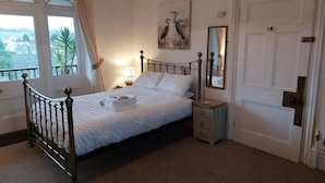 A neatly made bed with a headboard, a bedside table with a lamp, a mirror, and a door with a handle.