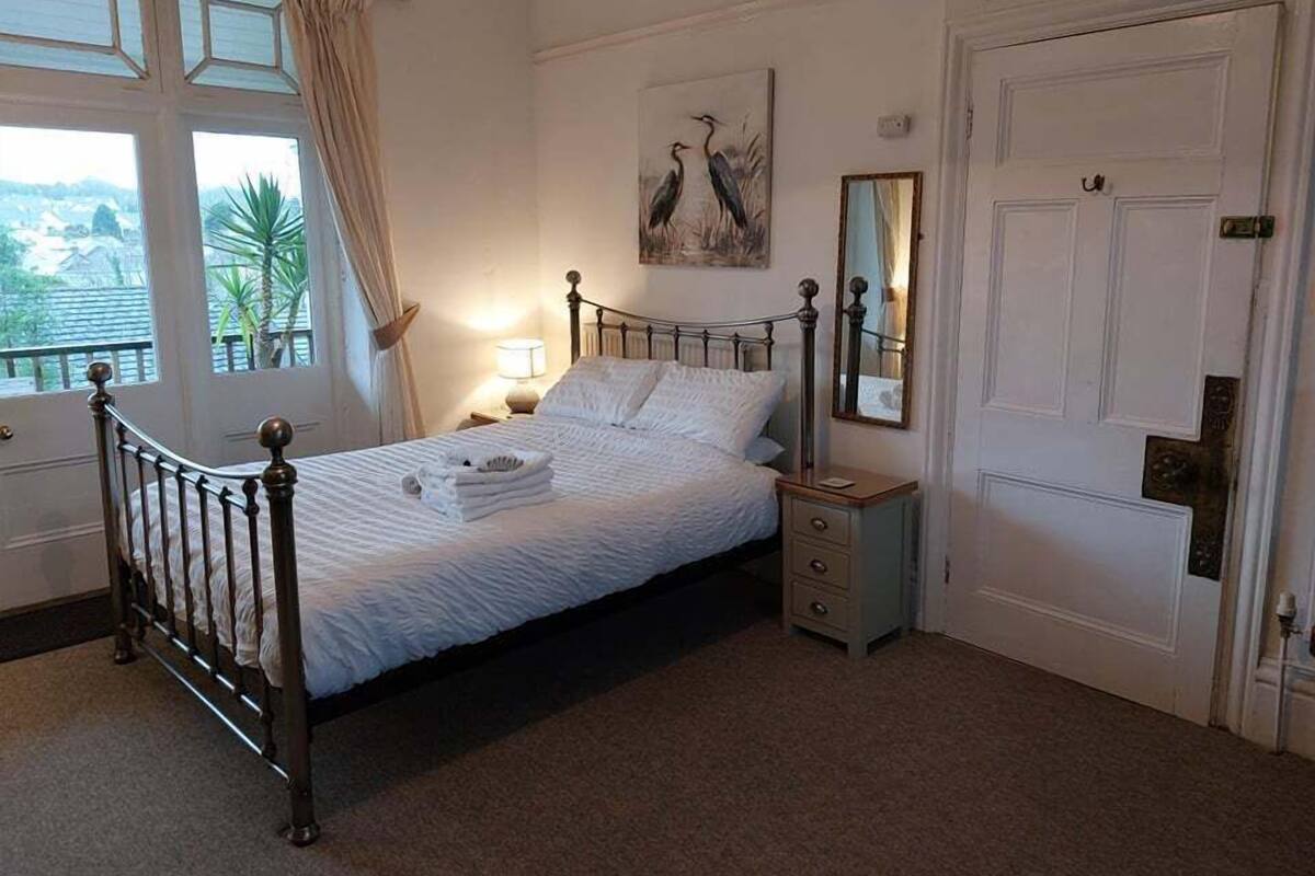 A neatly made bed with a headboard, a bedside table with a lamp, a mirror, and a door with a handle.