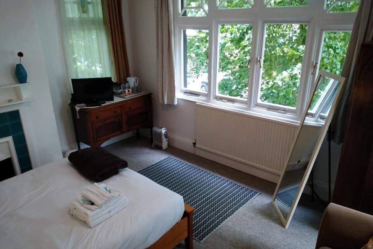 A bedroom with a bed, a dresser, a radiator, and a window with a view of greenery.