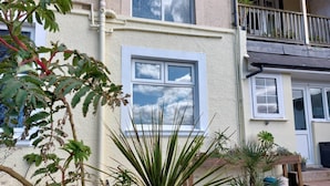 A residential building with a balcony, a window with a view of the sky, and various plants in the garden area.