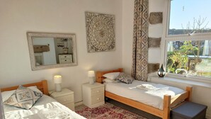 A bedroom with two wooden beds, a mirror, a decorative wall piece, and a window with a view of greenery.
