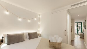 Cama bem arrumada com cabeceira, mesa de cabeceira com abajur e cesta de toalhas.