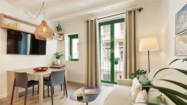 Quarto de hotel moderno com área de refeições, sofá, TV e varanda com cortinas.
