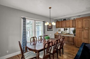 A dining area with a wooden table and chairs, a hanging light fixture, and wooden cabinets in the background.