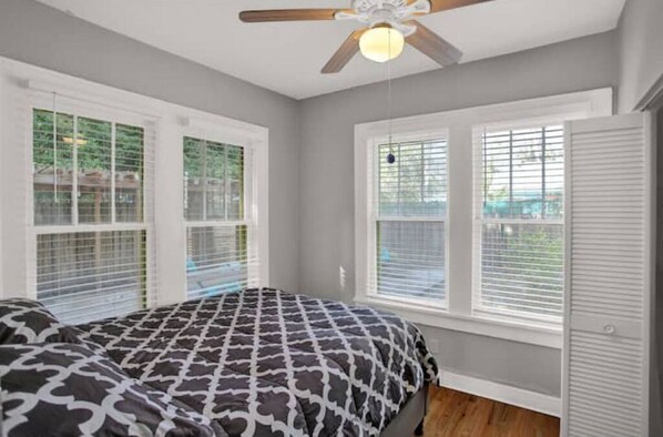 A bedroom with a bed, windows with blinds, a ceiling fan, and a door.