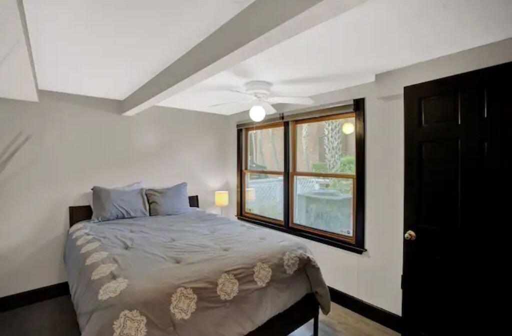 Un dormitorio con cama, ventana, ventilador de techo y puerta.