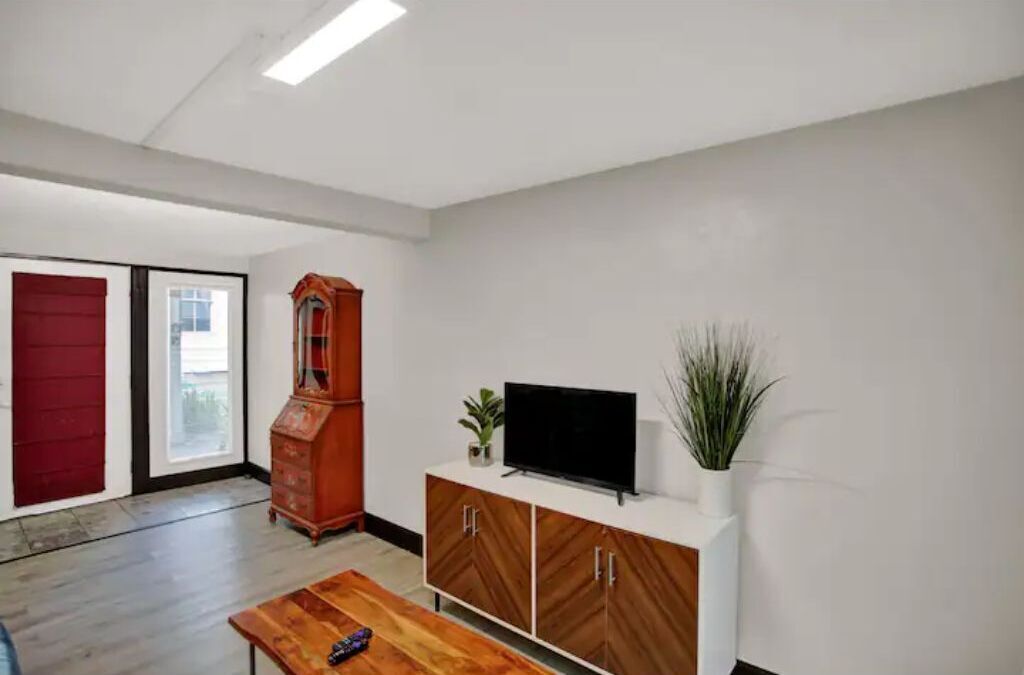 A room with a wooden cabinet, a flat-screen TV, and a red door.