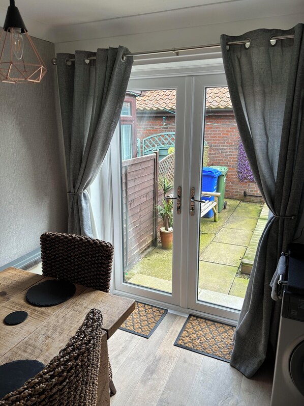 A room with a wooden table, a woven chair, and a sliding glass door leading to a garden. - Immaculate 2-bed Cottage in Flamborough (Bridlington)