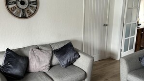 Ein Wohnzimmer mit grauem Sofa, zwei schwarzen Kissen und einer Wanduhr.
