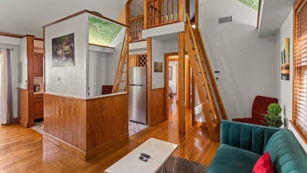 Un'ampia stanza in stile loft con una scala in legno, un comodo divano verde e un angolo cottura.