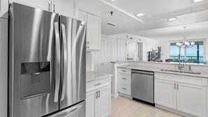 Una cocina moderna con electrodomésticos de acero inoxidable, armarios blancos y vistas al exterior.