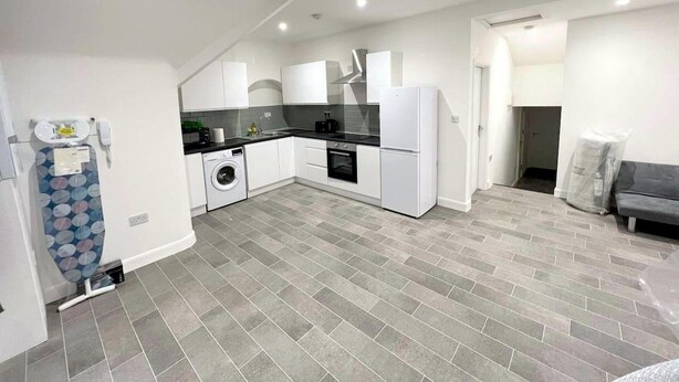 Une cuisine moderne avec des meubles blancs, un lave-linge et un sol carrelé de couleur grise.