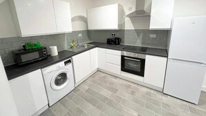 Une cuisine moderne avec des meubles blancs, un lave-linge, un four à micro-ondes, un grille-pain et un four encastré.