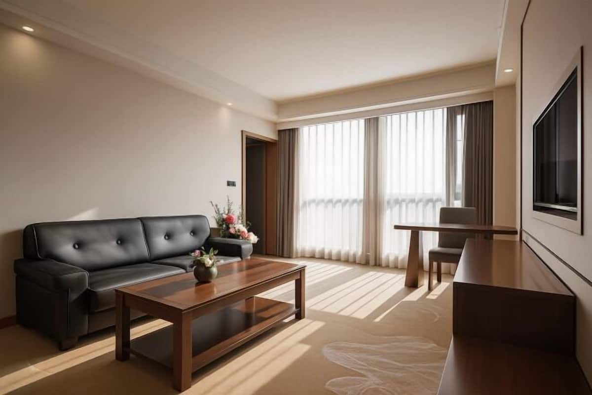 A modern hotel room with a sofa, a coffee table, a TV, and a large window with curtains.