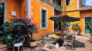 An outdoor patio with a table and chairs, surrounded by potted plants and a building with orange walls and green windows. - Yunqi Hotel (Kunming)