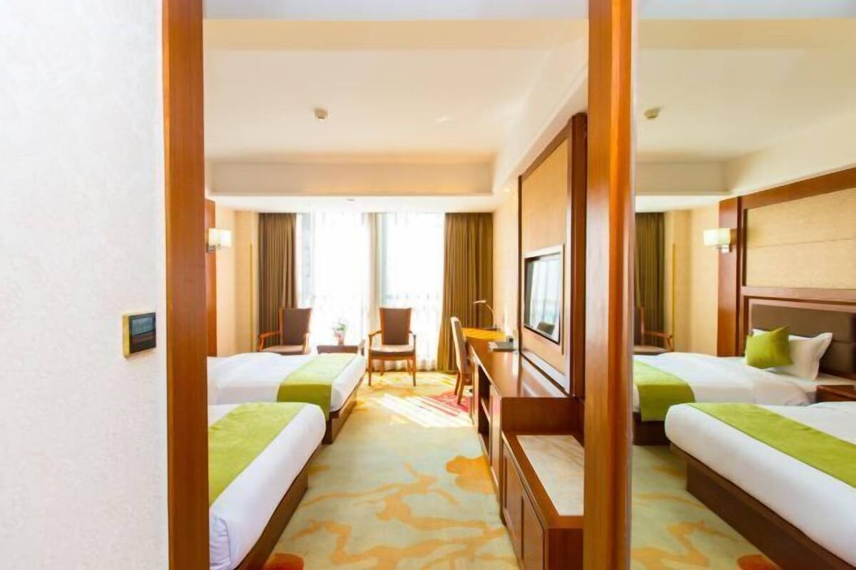 A hotel room with two beds, a desk, a chair, and a television.