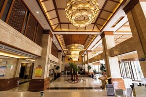 A spacious lobby with a high ceiling, a central chandelier, and a polished marble floor.