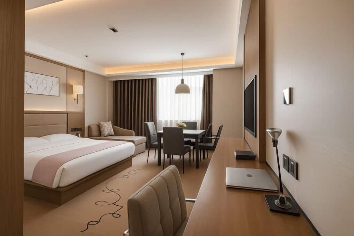 A hotel room with a bed, a desk, a chair, a TV, and a window with curtains.