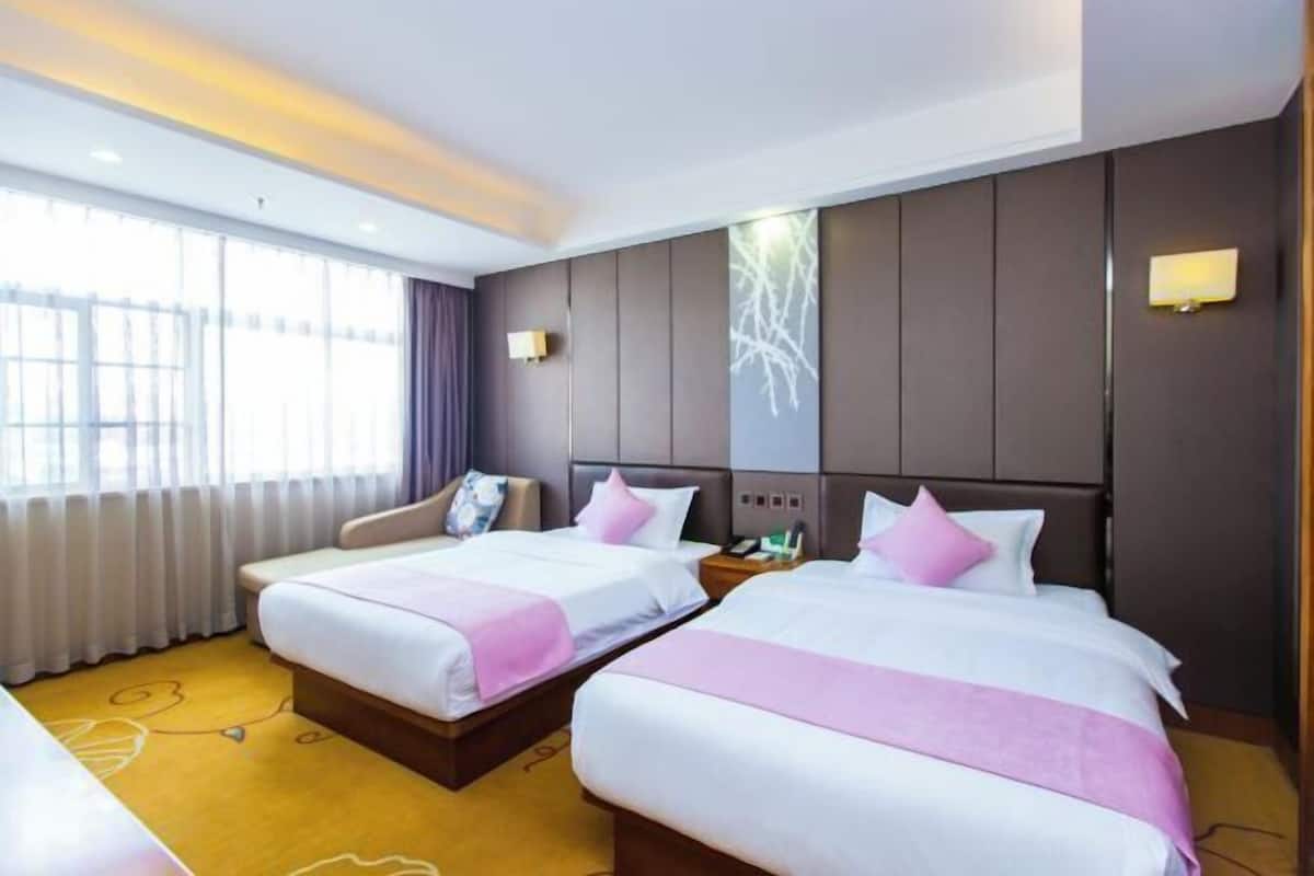 A hotel room with two beds, a sofa, a large window with curtains, and a wall-mounted TV.