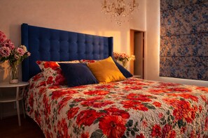 A bedroom with a tufted headboard, floral bedding, and a chandelier. - Charming Metro Santa Ana 2 bedrooms (Santiago)