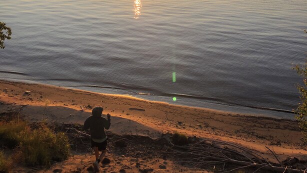 A sunset over a calm lake with a person running along the shore.