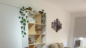 Una sala de estar moderna con suelo de madera, un sofá blanco, una silla blanca, un escritorio con una computadora portátil y una estantería con plantas.