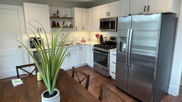 Une cuisine moderne avec des meubles blancs, des appareils en acier inoxydable et une table à manger en bois.