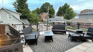 Une terrasse avec des meubles d’extérieur, un barbecue et un tapis à motifs.