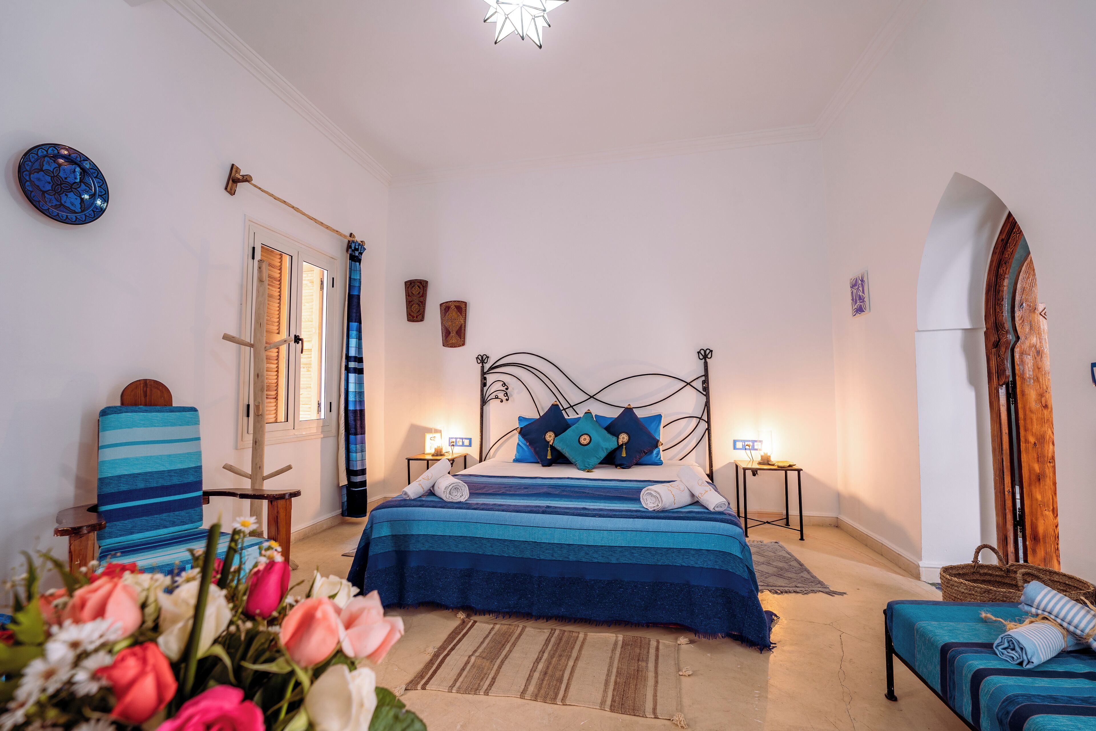 A bedroom with a bed, a chair, a bedside table, a lamp, and a wooden door.