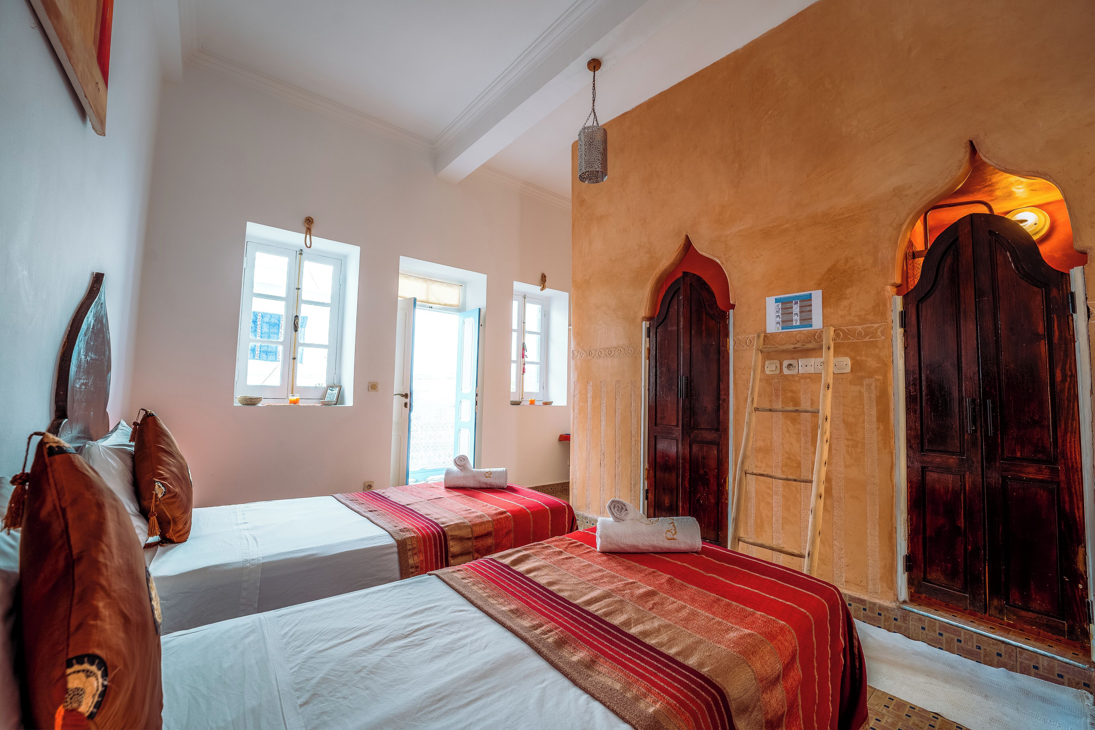 Habitación de hotel con dos camas, un armario de madera, una ventana y un aplique de pared.
