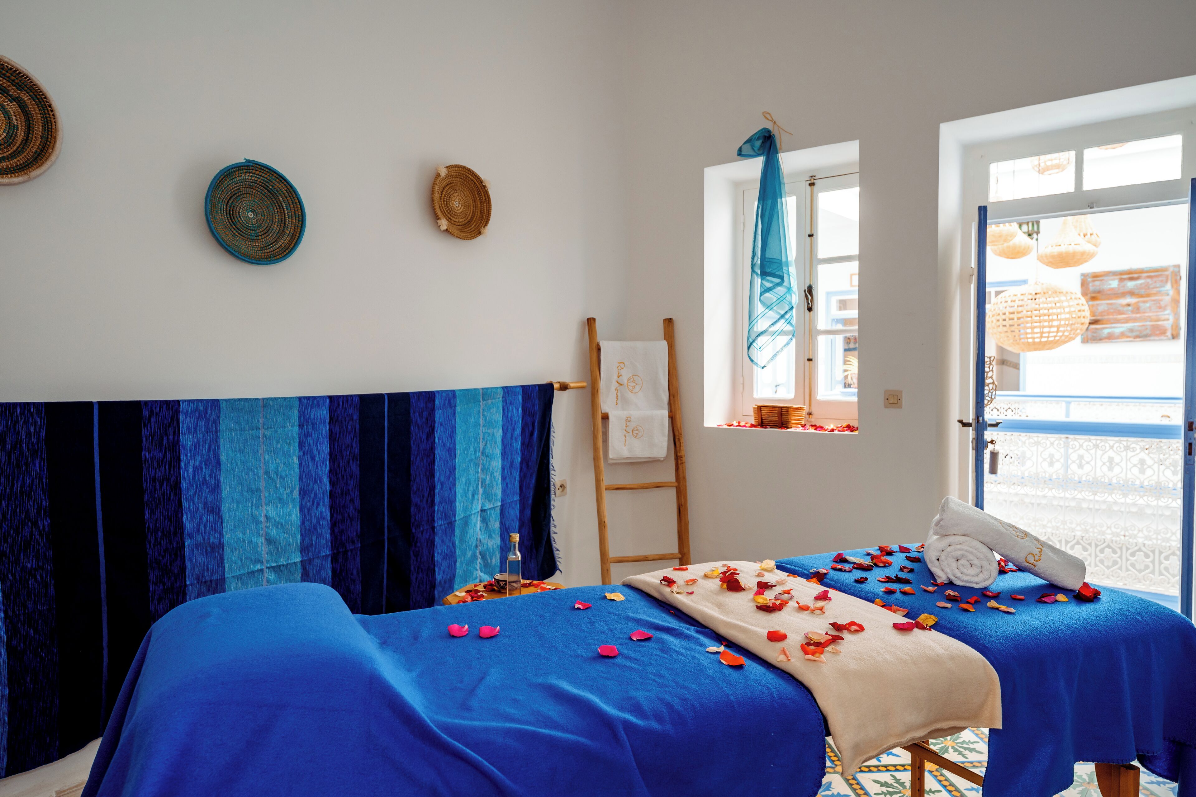 Habitación con dos camas cubiertas con sábanas azules, una escalera de madera y una ventana con vistas.