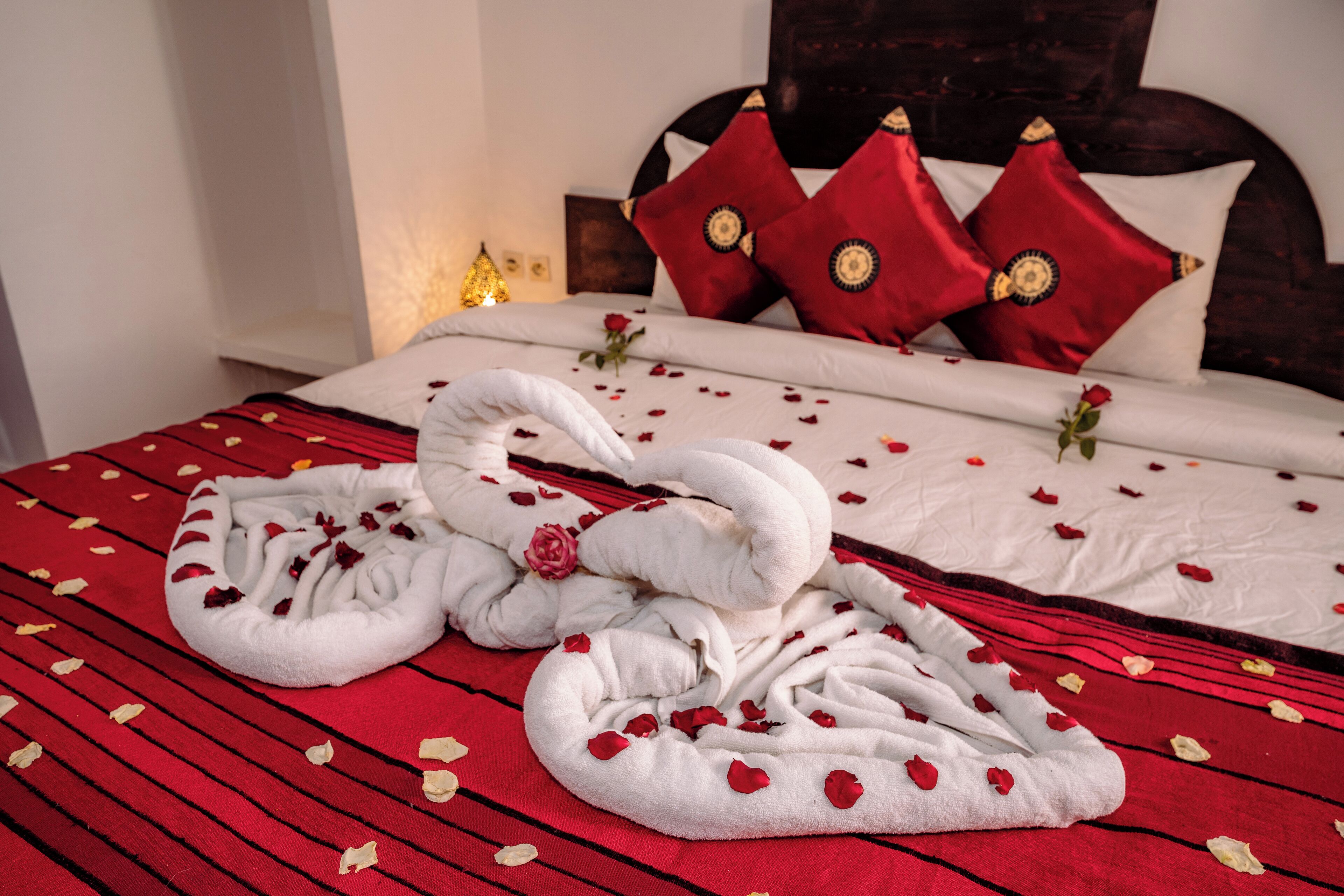 Una cama bien hecha adornada con pétalos de rosa y una disposición de toallas con forma de cisne.