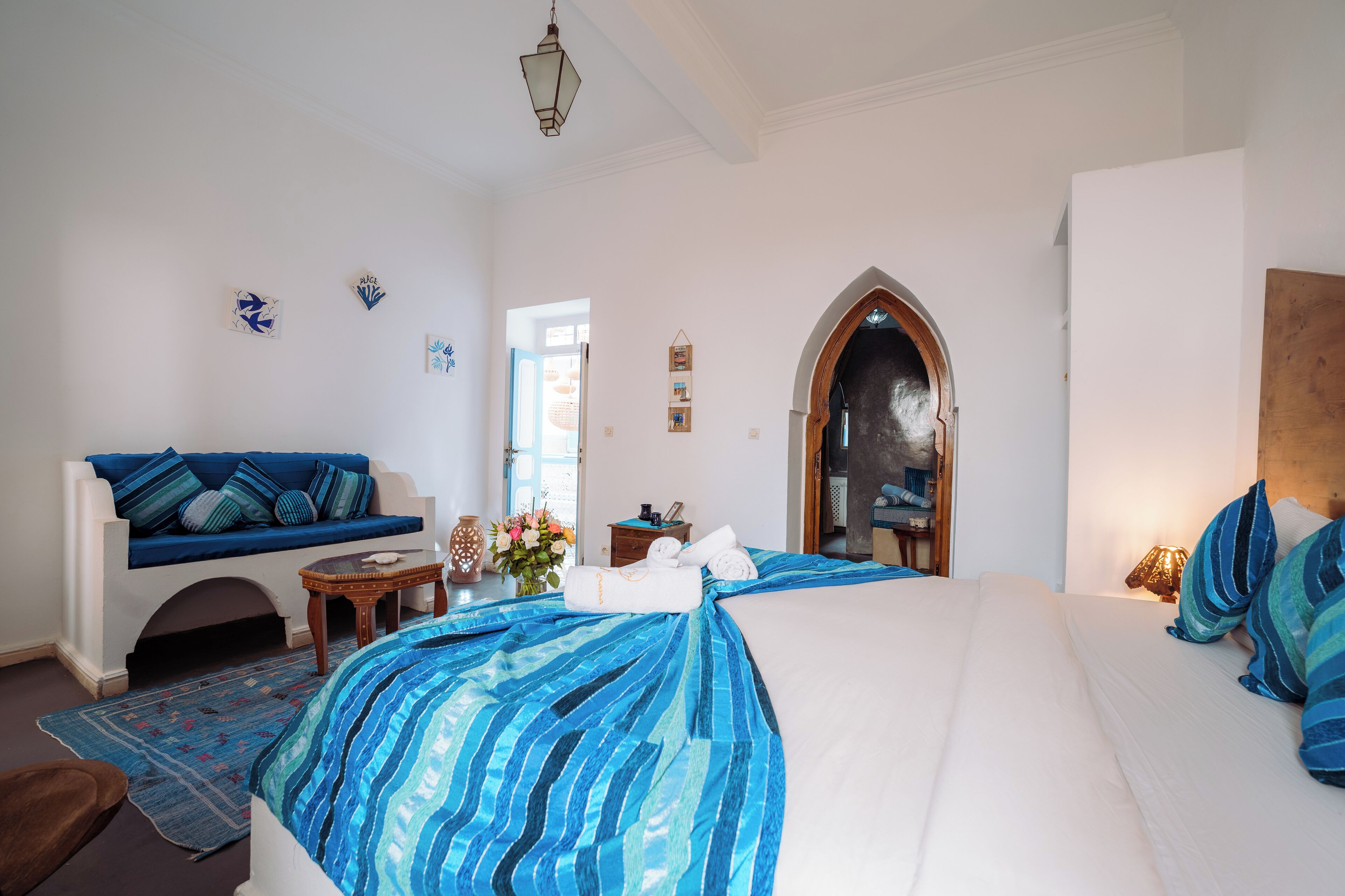 A bedroom with a large bed, a sofa, a small table with a vase, and a mirror.