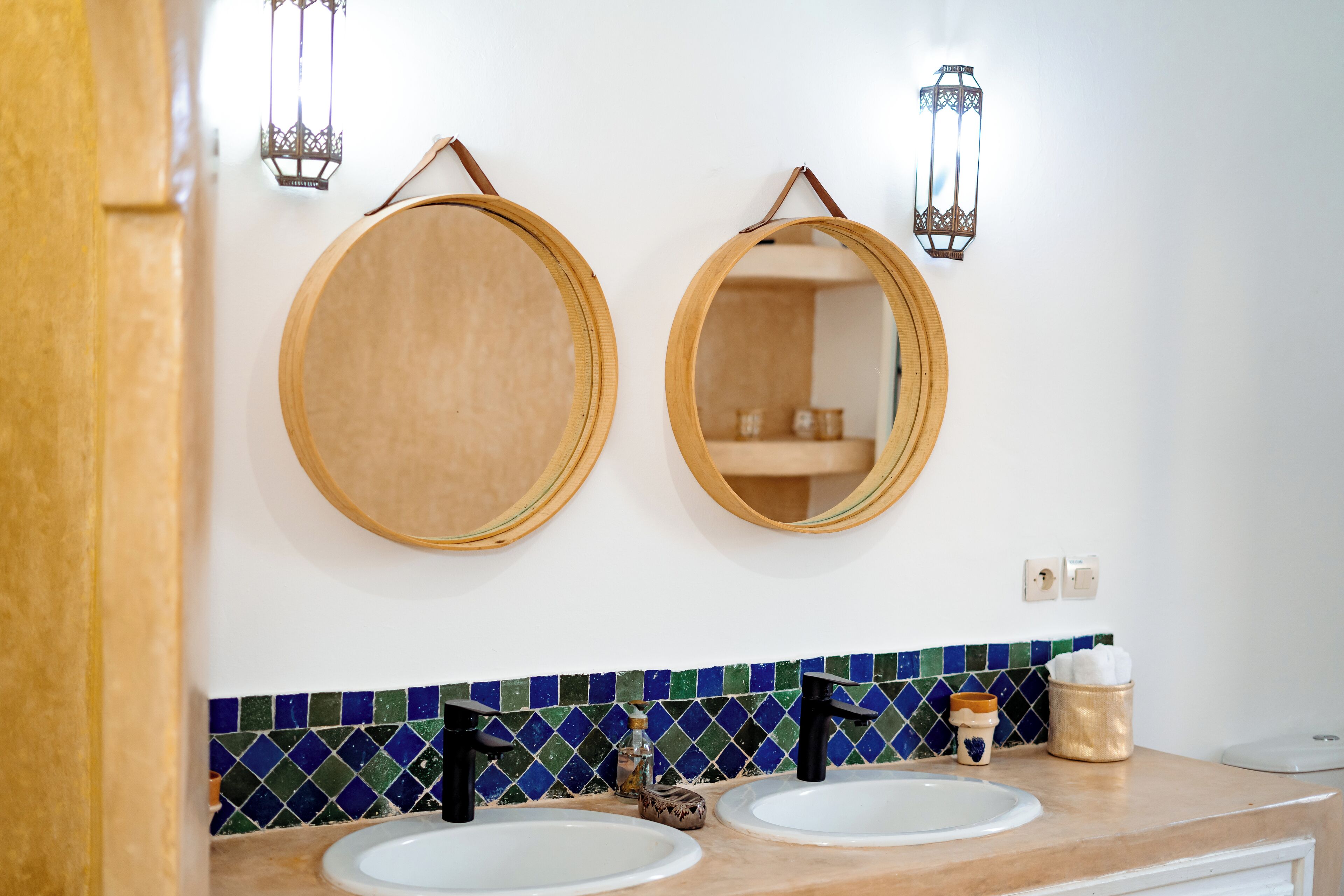 Un baño con dos espejos redondos, un salpicadero de azulejos y una encimera con dos lavamanos y artículos de aseo.