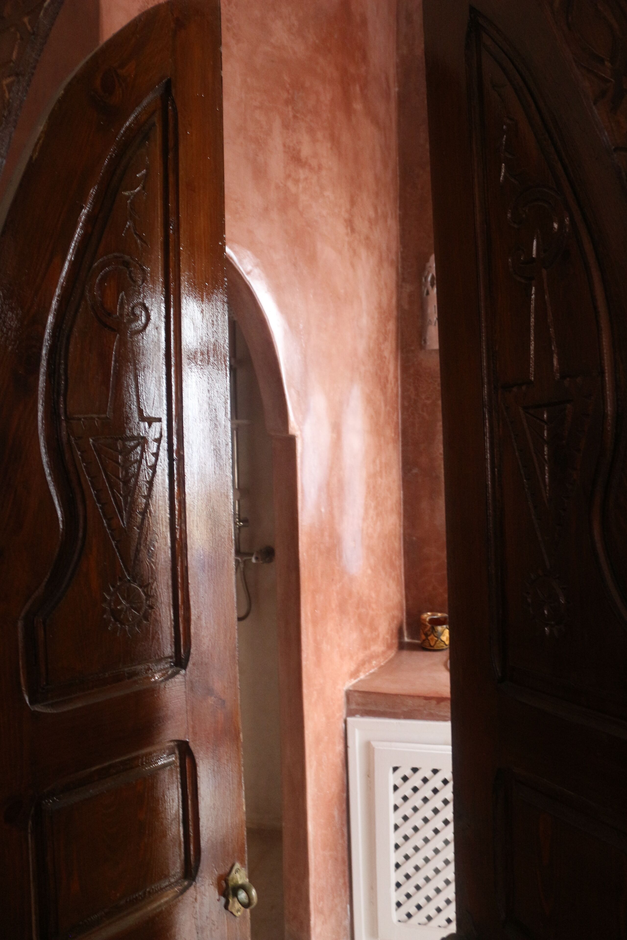 A wooden door with intricate carvings, a white wall with a textured pattern, and a small brass door handle.