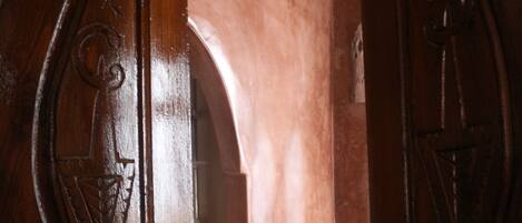 A wooden door with intricate carvings, a white wall with a textured pattern, and a small brass door handle.