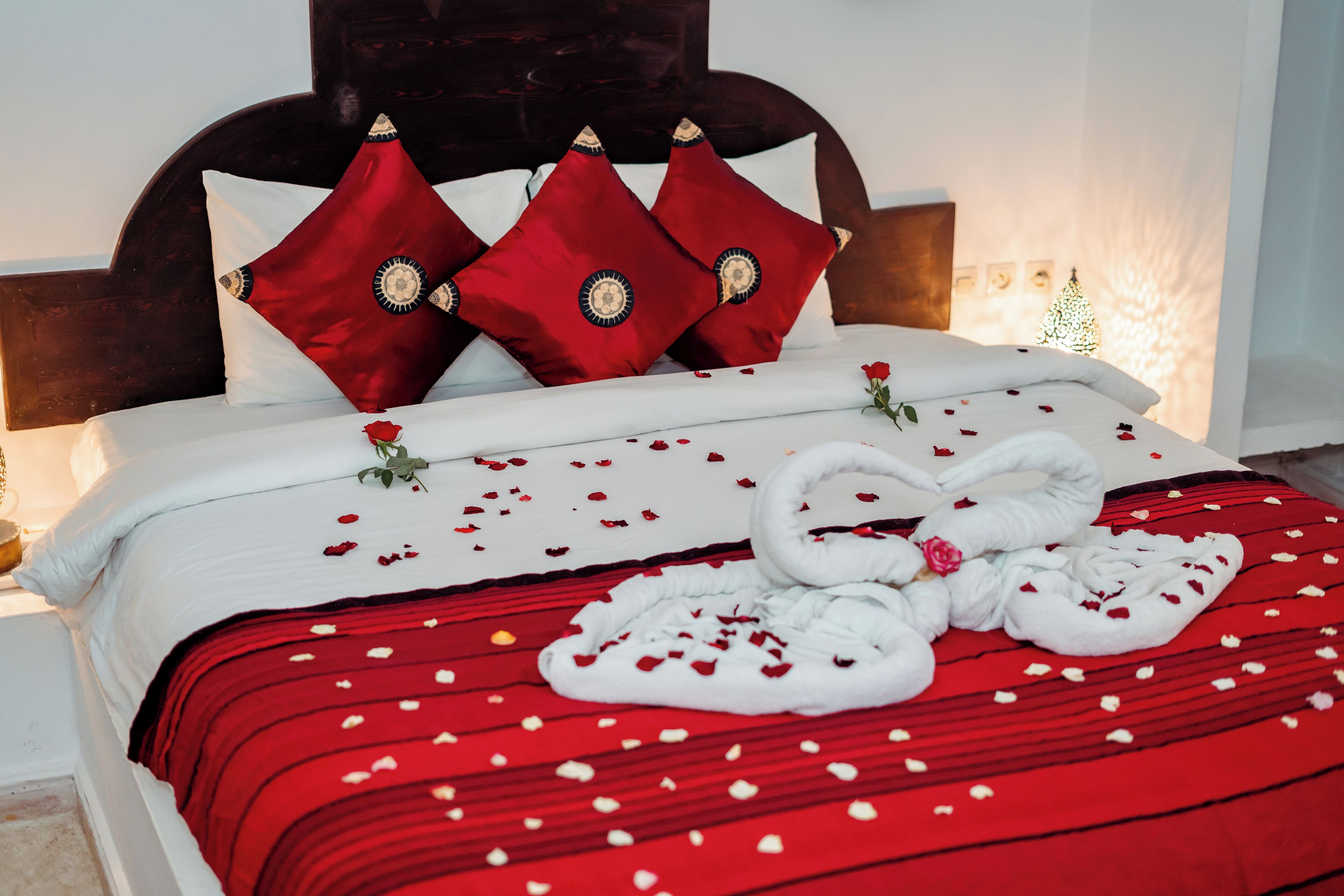 Un lit bien fait, avec une literie rouge et blanche, une tête de lit en bois et des coussins décoratifs.