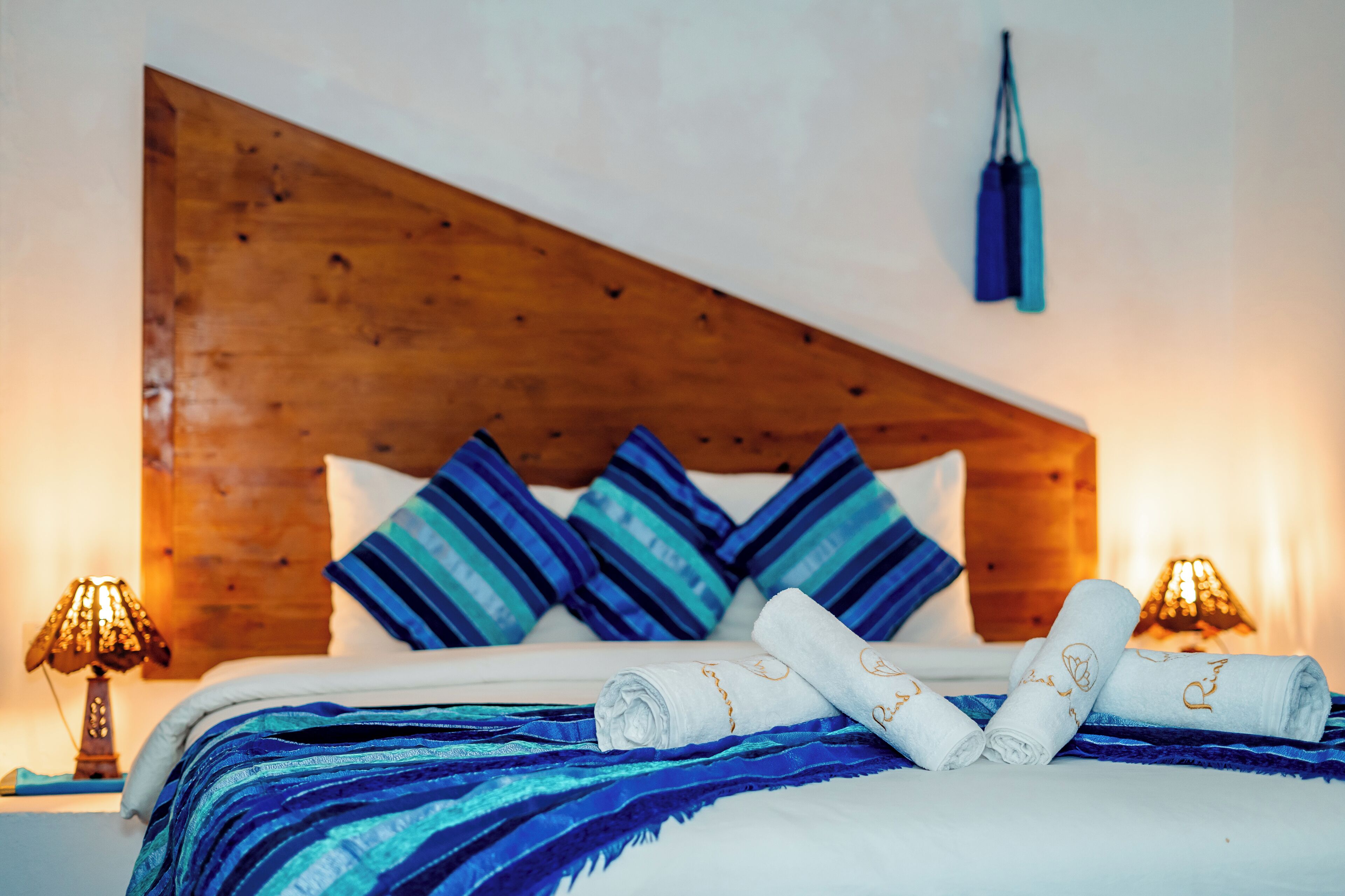 A neatly made bed with blue and white striped pillows, a wooden headboard, and two bedside lamps.