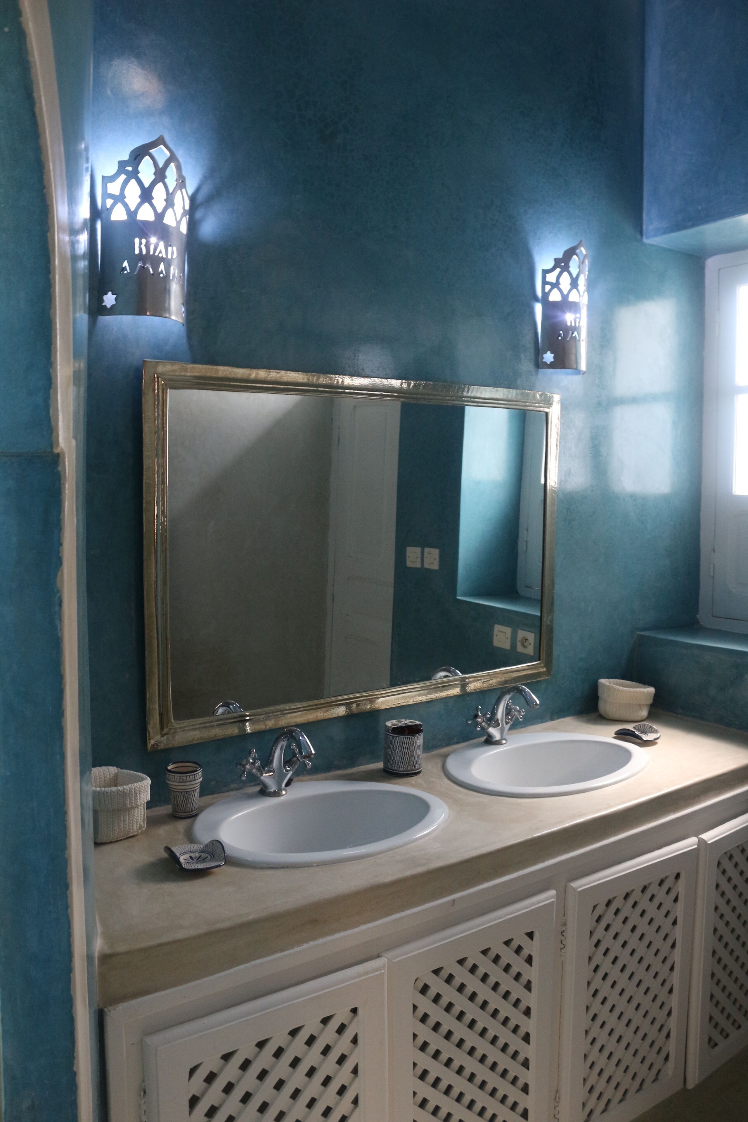A bathroom with two sinks, a large mirror, and decorative wall sconces.