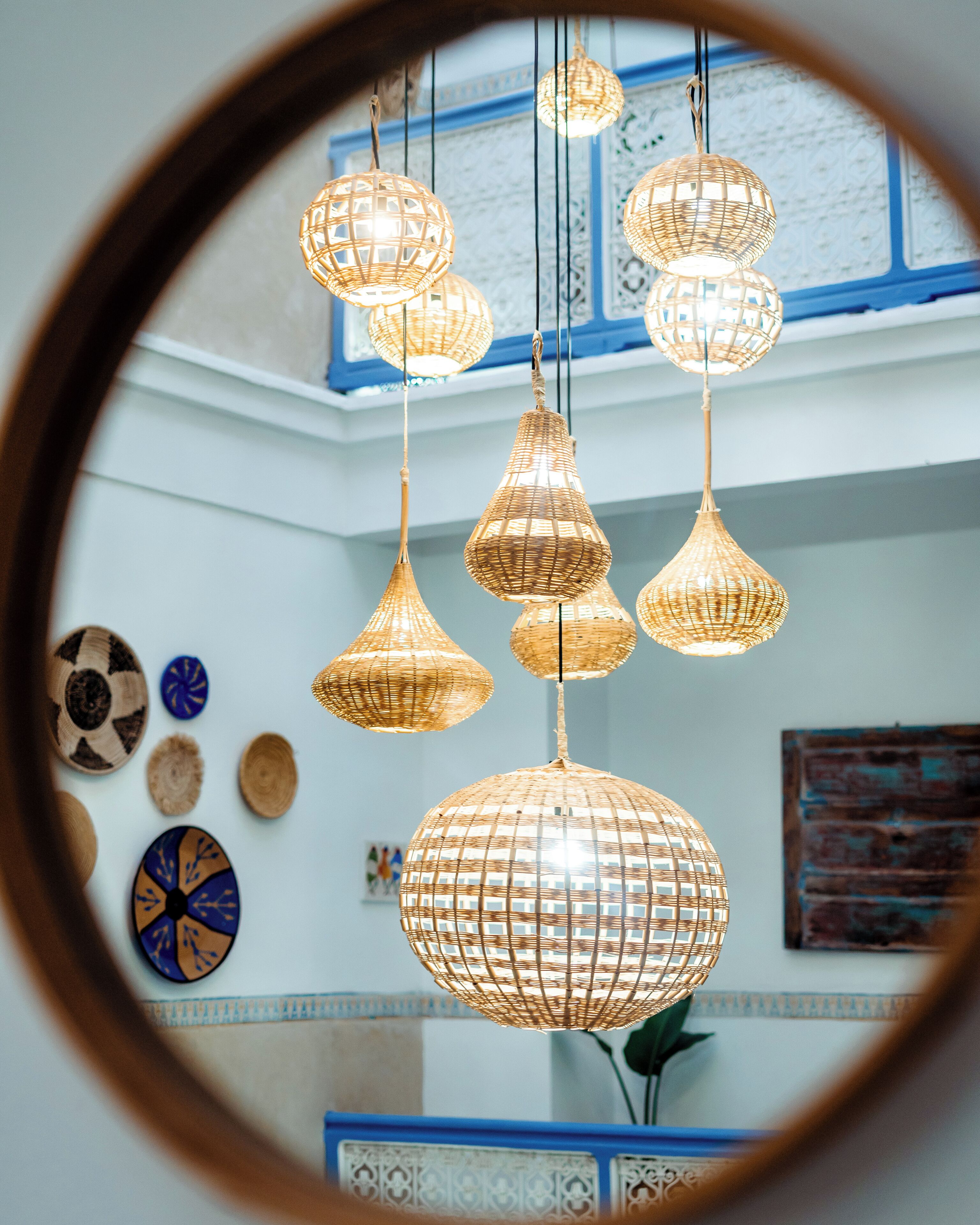 A room with hanging wicker chandeliers, a blue-framed window, and decorative plates on the wall.