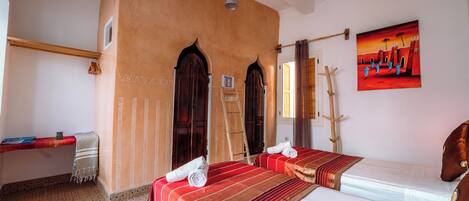 A hotel room with two beds, a wooden ladder, a red and white striped bedspread, and a painting of a sunset scene.