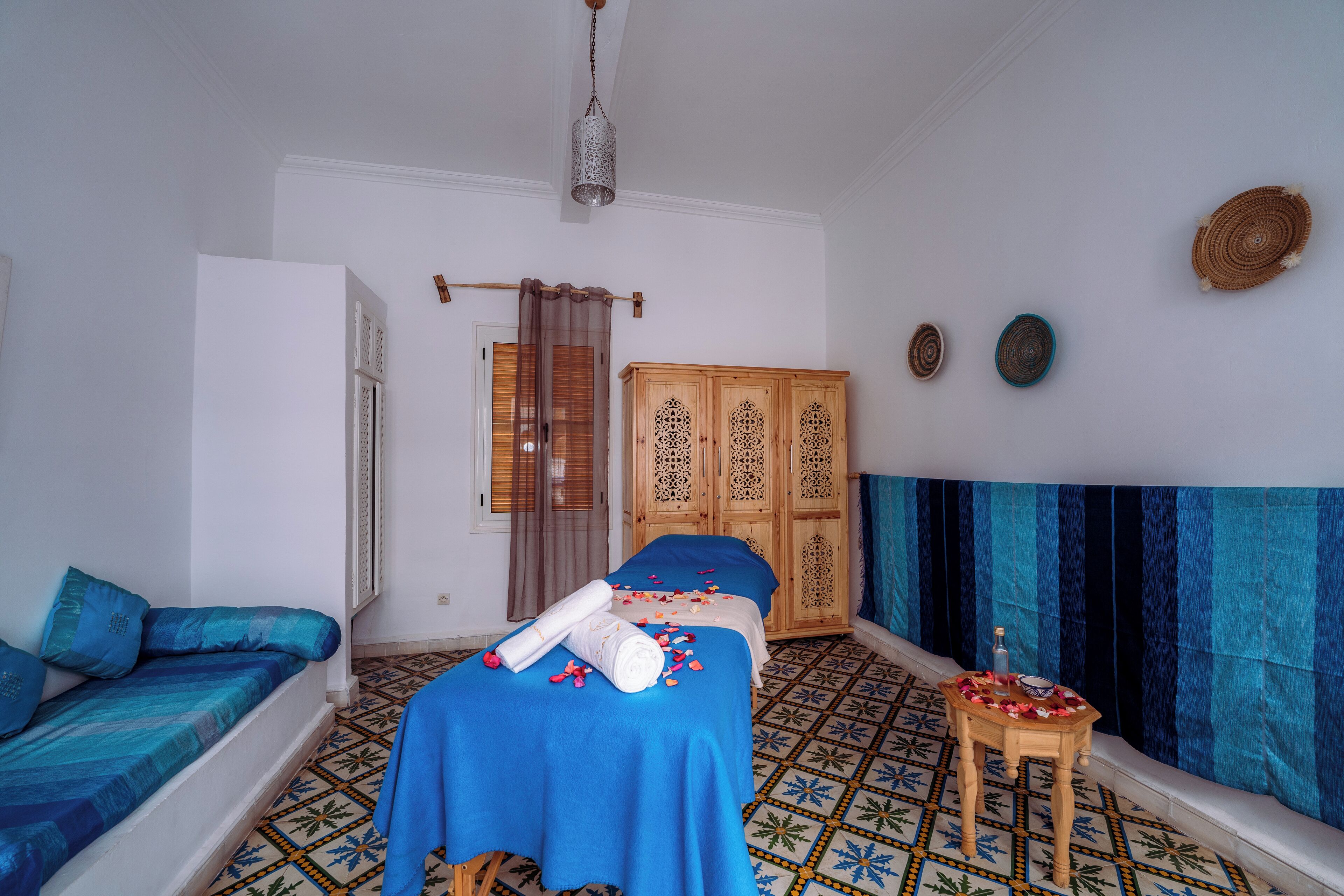 A room with a bed, a wooden cabinet, a small table with a bottle, and a patterned floor.