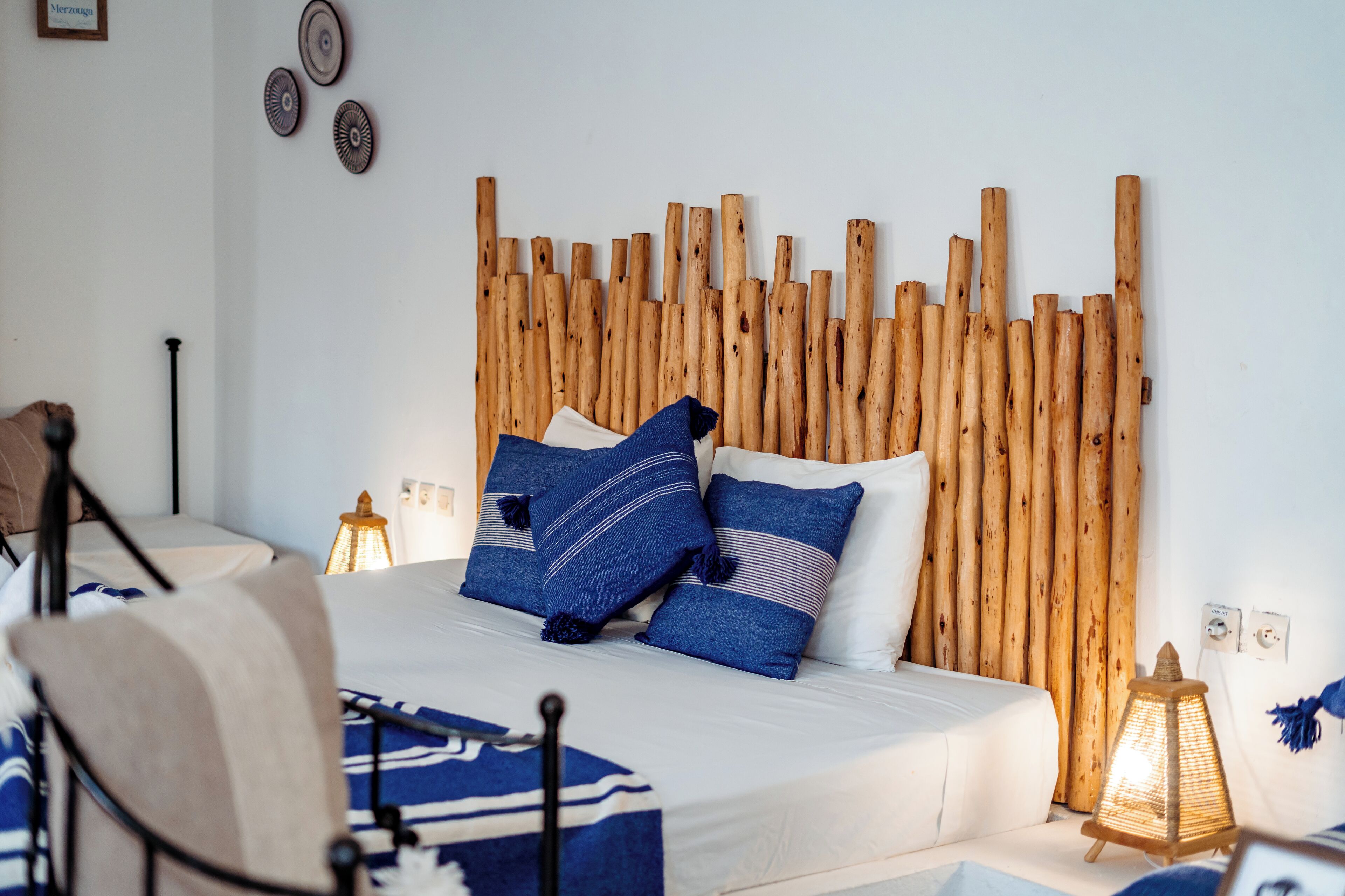 Un dormitorio con cabecera de madera, cama con ropa de cama azul y blanca, y una mesita de noche con lámpara.