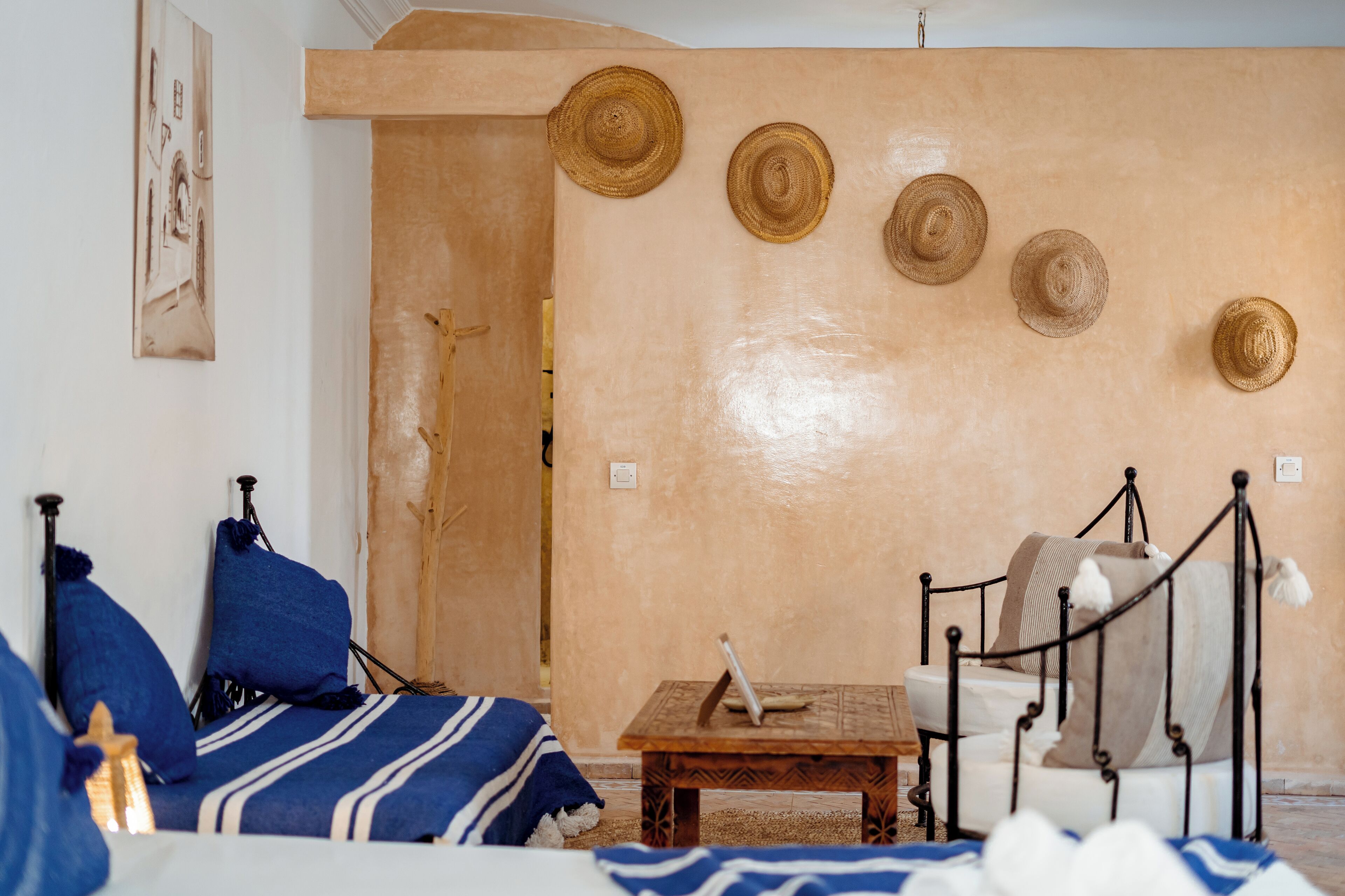 A room with a bed, a small table, and a wall with hats.