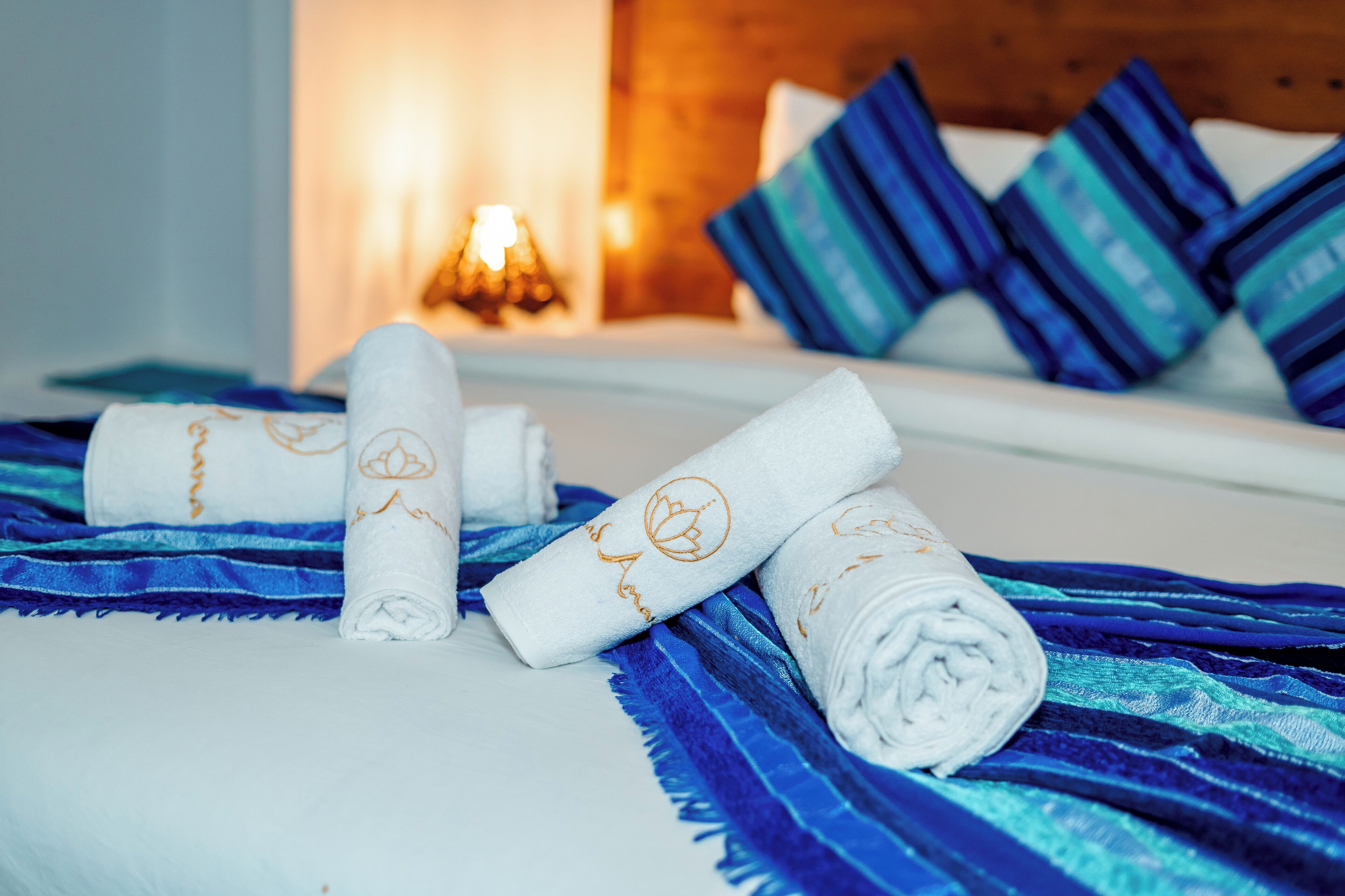 A neatly made bed with rolled white towels and blue striped blankets, a bedside lamp, and blue pillows.