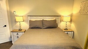 A neatly made bed with a quilted cover, flanked by two bedside tables with lamps, in a room with a simple, clean design. - Modern 1 Bedroom, 10 minute walk to Downtown (Moncton)