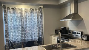 A modern kitchen with a central island, stainless steel appliances, and a patterned curtain. - Modern 1 Bedroom, 10 minute walk to Downtown (Moncton)
