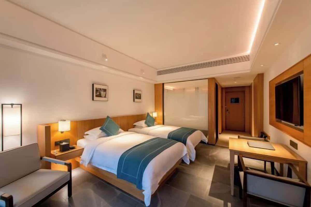 Habitación de hotel con dos camas, un escritorio, una silla, un televisor y una mesita de noche con lámpara.