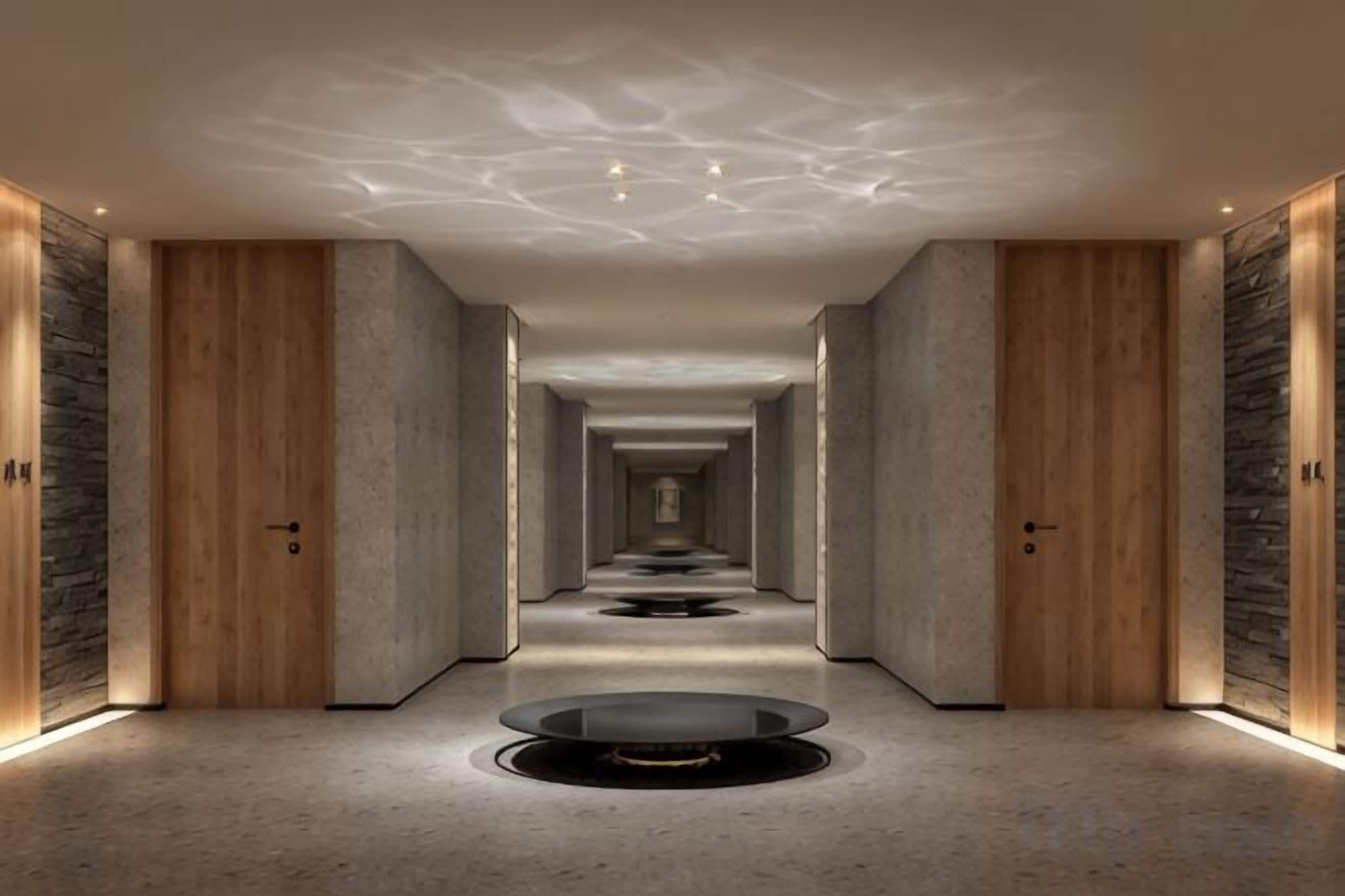 A hotel corridor with a central circular feature, wooden doors, and a patterned ceiling.